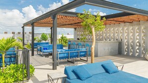 Eine Dachterrasse mit blauen Sitzgelegenheiten, einer Pergola und Blick auf die Stadtlandschaft.