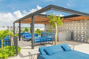 Een terras op het dak met blauwe zitplaatsen, een pergola en uitzicht op de stad.