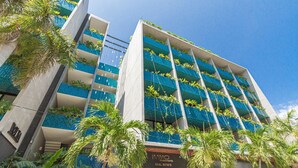 Ein mehrstöckiges Hotel mit Balkonen, die mit Pflanzen geschmückt sind, einem klaren blauen Himmel und Palmen im Vordergrund.