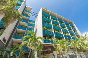 Een meerhoog hotel met balkons versierd met planten, een helderblauwe lucht en palmbomen op de voorgrond.