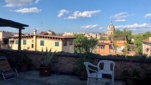 A rooftop terrace with potted plants, a chair, and a view of a cityscape including a prominent dome structure. - Sant'Onofrio - Trastevere Vatican apartment in Rome (Roma)