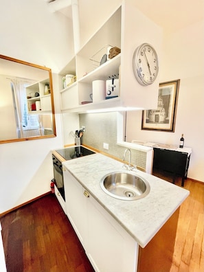 A modern kitchen with a marble countertop, stainless steel sink, and a built-in oven. There is a clock on the wall and a framed picture above the sink. - Sant'Onofrio - Trastevere Vatican apartment in Rome (Roma)