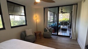 Una camera da letto con un letto grande, una ventola a soffitto, una finestra con persiane e vista su un patio esterno arredato.