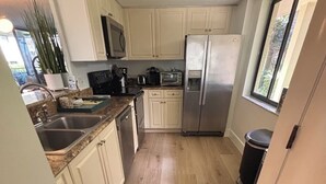 Una cucina compatta con pavimento in legno, pensili bianchi, frigorifero in acciaio inossidabile e forno a microonde.