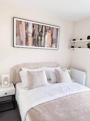 A modern bedroom with a large bed, white bedding, a headboard, a bedside table with a lamp, and a framed abstract painting above the bed. - Spacious 2BR Home | 3 Parking | Offers Weekly Stay (Reading)
