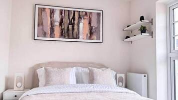 A modern bedroom with a large bed, a wall-mounted abstract painting, and built-in shelving with decorative items.