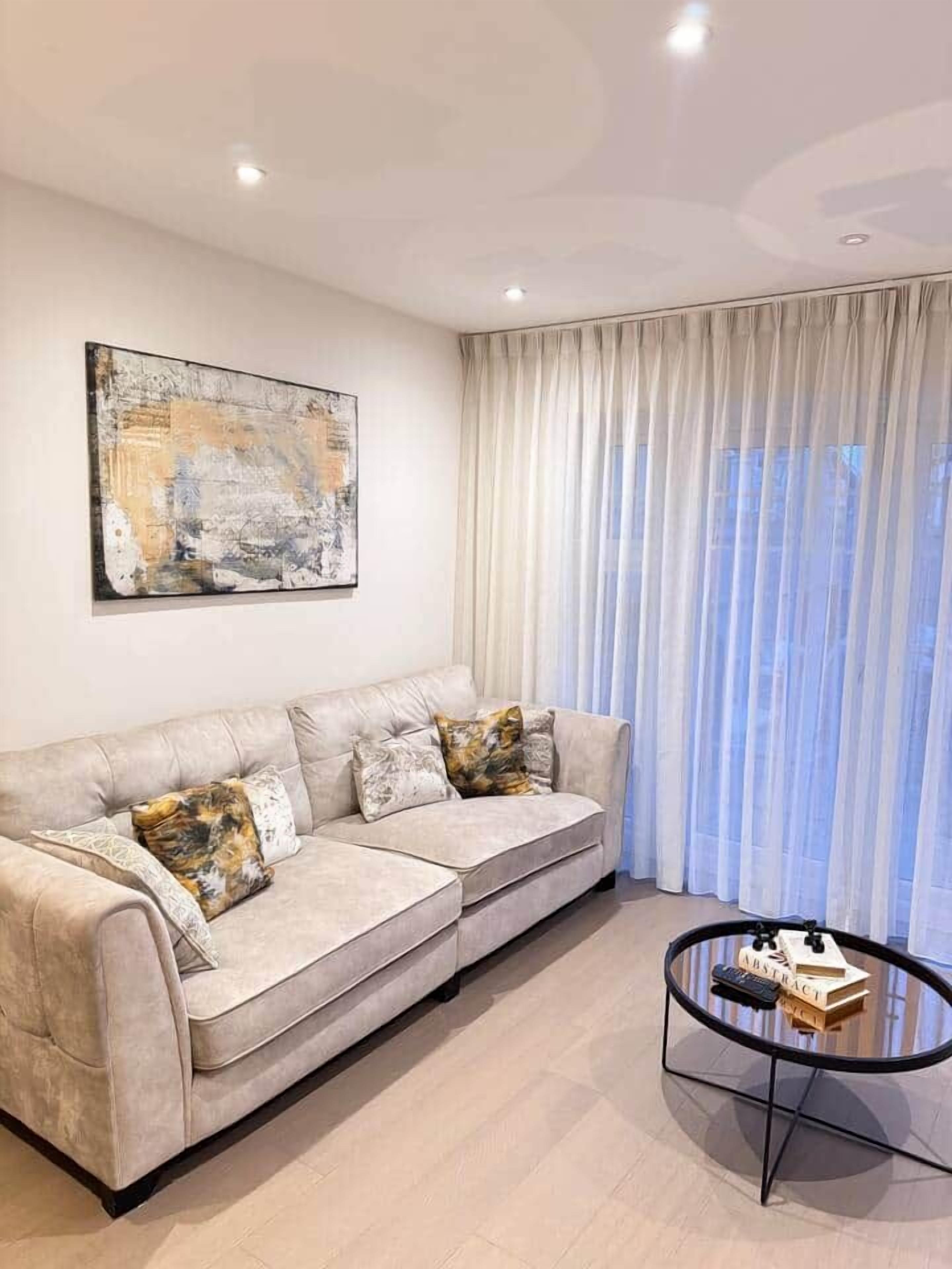 Un salon moderne avec un canapé d’angle beige, une table basse en verre et un grand tableau abstrait accroché au mur.