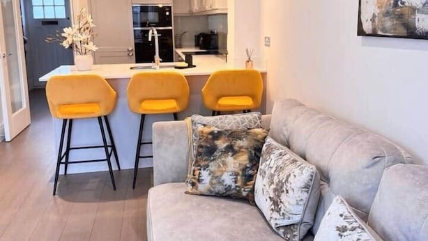 A modern kitchen with white cabinets, a central island, and yellow bar stools. - Spacious 3BR Home | 3 Parking | Offers Weekly Stay (Reading)