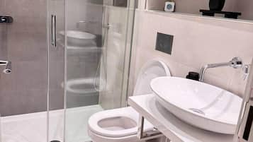 Un baño moderno con ducha envuelta en vidrio, inodoro blanco y lavamanos grande.