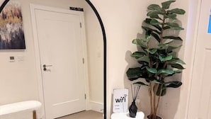 A hallway with a white door, a bench, a large mirror, a potted plant, and a 'wifi' sign. - Spacious 3BR Home | 3 Parking | Offers Weekly Stay (Reading)