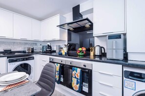 Eine moderne Küche mit weißen Schränken, einem Geschirrspüler, einer Waschmaschine und einer Kaffeemaschine.
