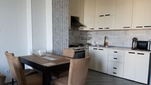 Eine moderne Küche mit weißen Schränken, einem Herd und einer Mikrowelle. Ein Esstisch mit Stühlen steht ebenfalls dort.