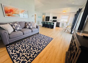 Ein modernes Wohnzimmer mit grauem Sofa, einem gemusterten Teppich und einer Küche im Hintergrund.