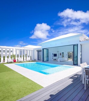 Een modern huis met een zwembad, terras en een overdekte zitplek buiten.