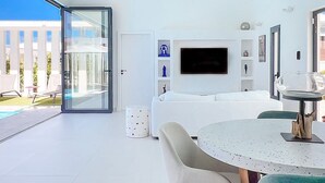 A modern living room with a large TV, a dining area with a round table, and a glass door leading to an outdoor patio. - Villa SANDI luxury and comfort - a contemporary oasis. Ideal for vacations (Saint-François)