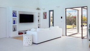 A spacious living room with a white sofa, a flat-screen TV, and a ceiling fan. - Villa SANDI luxury and comfort - a contemporary oasis. Ideal for vacations (Saint-François)