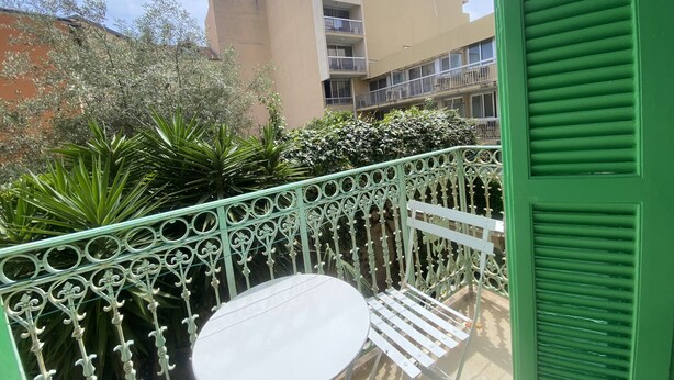 A balcony with a white table and chairs, surrounded by green metal railings and potted plants. - Apartment Iris II - Menton City Centre (Menton)
