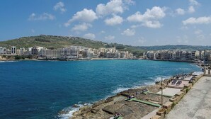 A coastal cityscape with buildings along the waterfront, a rocky shoreline, and a clear blue sky. - Sea view two bedroom apartment (Marsalforn)