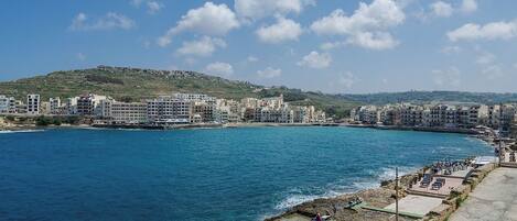 A coastal cityscape with buildings along the waterfront, a rocky shoreline, and a clear blue sky.