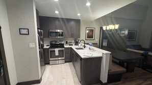 A modern kitchen with stainless steel appliances, a marble countertop, and a dining area with a wooden table and bench. - Park City, Ski-in, Ski-out, 2-bed 2 bath, Sleeps 8 (Park City)