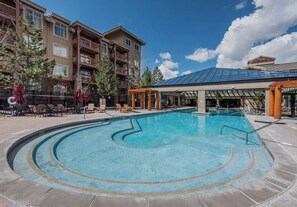 A swimming pool with a sunshade structure, lounge chairs, and a building with multiple balconies in the background. - Park City, Ski-in, Ski-out, 2-bed 2 bath, Sleeps 8 (Park City)