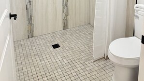 Ein Badezimmer mit Dusche, gefliestem Boden und Toilette.