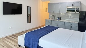 Ein modernes Hotelzimmer mit einem großen Bett, einem flachbildfernseher an der Wand, einer Küchenzeile mit grauen Schränken und einem Holzboden.