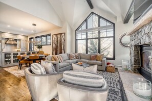 A spacious living room with a large sectional sofa, a fireplace, and a dining area with a table and chairs. - CRBC - Ski-In/Ski-Out Arrowhead Penthouse 3BR 3.5BA Corner Unit Mountain Views (Edwards)