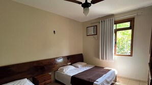 Habitación de hotel con dos camas, un ventilador de techo, una ventana con cortinas y un radio instalado en la pared.