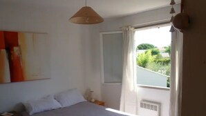 Ein Schlafzimmer mit einem Bett, einem Fenster mit Vorhängen, einer Hängeleuchte und einer Wand-Klimaanlage.