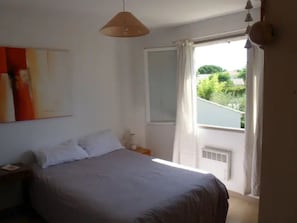Une chambre à coucher avec un lit, une fenêtre avec des rideaux, un luminaire suspendu et un appareil de climatisation fixé au mur.