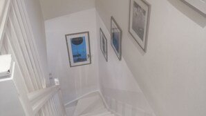 Eine Treppe mit weißen Geländern und einer Handlauf, die zu einer Zwischenebene mit gerahmten Bildern an der Wand führt.