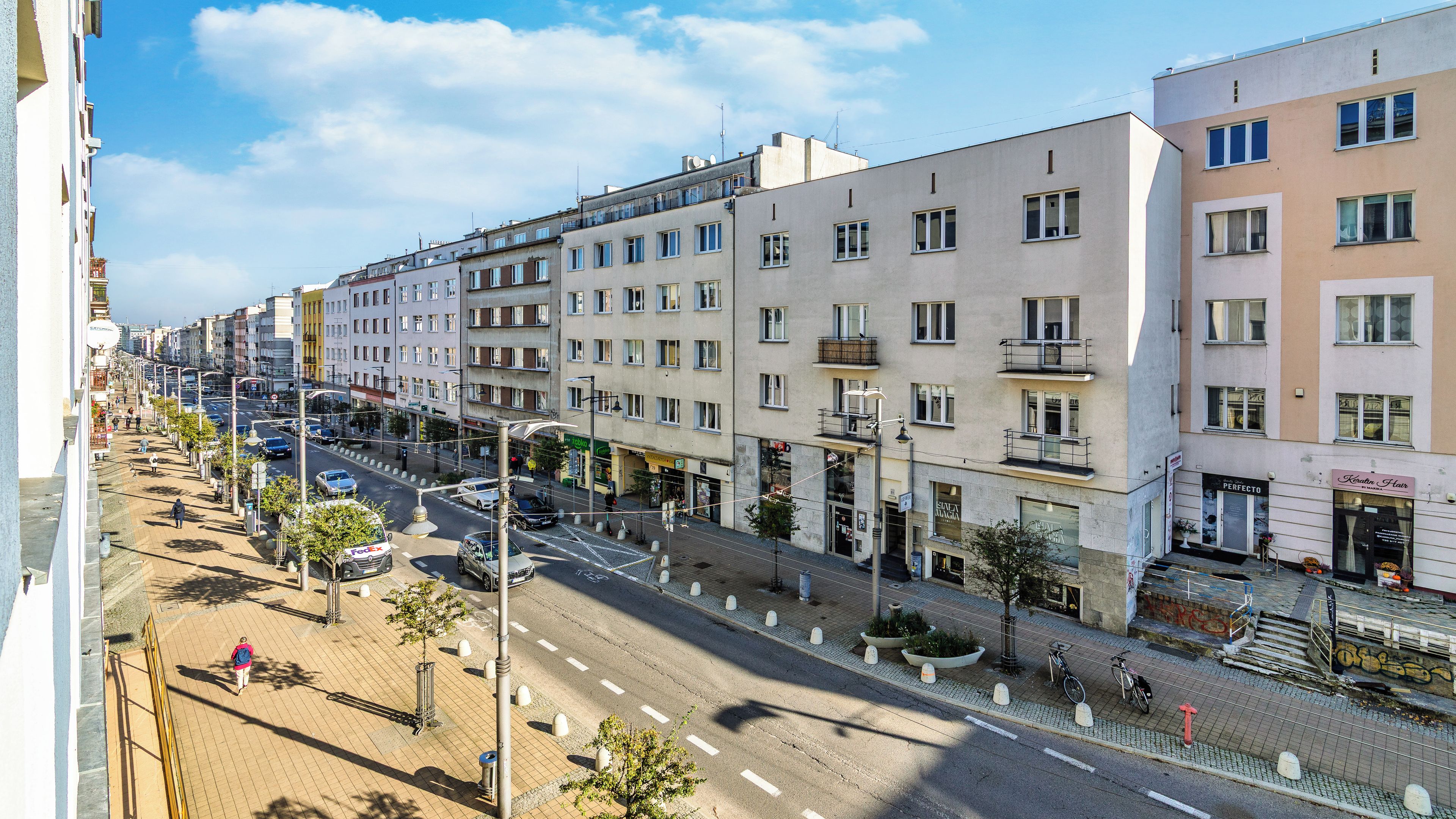 A multi-story building with a ground-floor commercial space, a pedestrian sidewalk, and a street with cars.