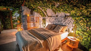A bedroom with a bed, a nightstand, and a wall with greenery. - Junglecavern - Private spa, unusual accommodation (Albertville)