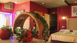 A hotel room with a bed, a large potted plant, a decorative archway, and a window with curtains. - Habitación con jacuzzi Paraiso del Sur (Cuernavaca)