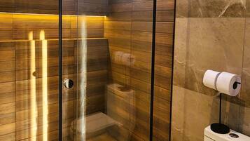 Ein modernes Badezimmer mit einer gläsernen Duschkabine, Holzpaneelen und einem WC mit Papierhalter.