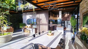 Een moderne keuken met een groot schiereiland, inbouwapparatuur en een eethoek met een marmeren tafel en stoelen.