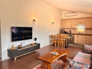 A modern living room with a flat-screen TV, wooden furniture, a dining area, and a kitchen with wooden cabinets. - Detached Single - Storey Stone House in Datça Karaincir - Karaincir Houses 2 (Muğla)