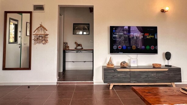 Una sala moderna con un televisor de pantalla plana montado en la pared, una mesa de centro de madera y un mueble bajo de madera oscura con objetos decorativos.