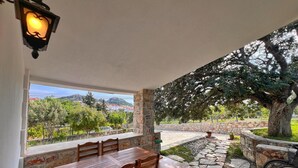 Un espacio de comedor al aire libre cubierto, con paredes de piedra, una mesa, sillas y vistas a un paisaje montañoso.