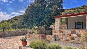 Un edificio de piedra con techo rojo, rodeado por un muro de piedra y macetas con plantas.