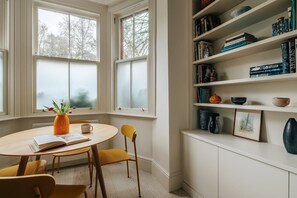 A cozy reading nook with a round table, chairs, and a bookshelf filled with books and decorative items. - Hampstead Heath Stylish Heathside Retreat (London)