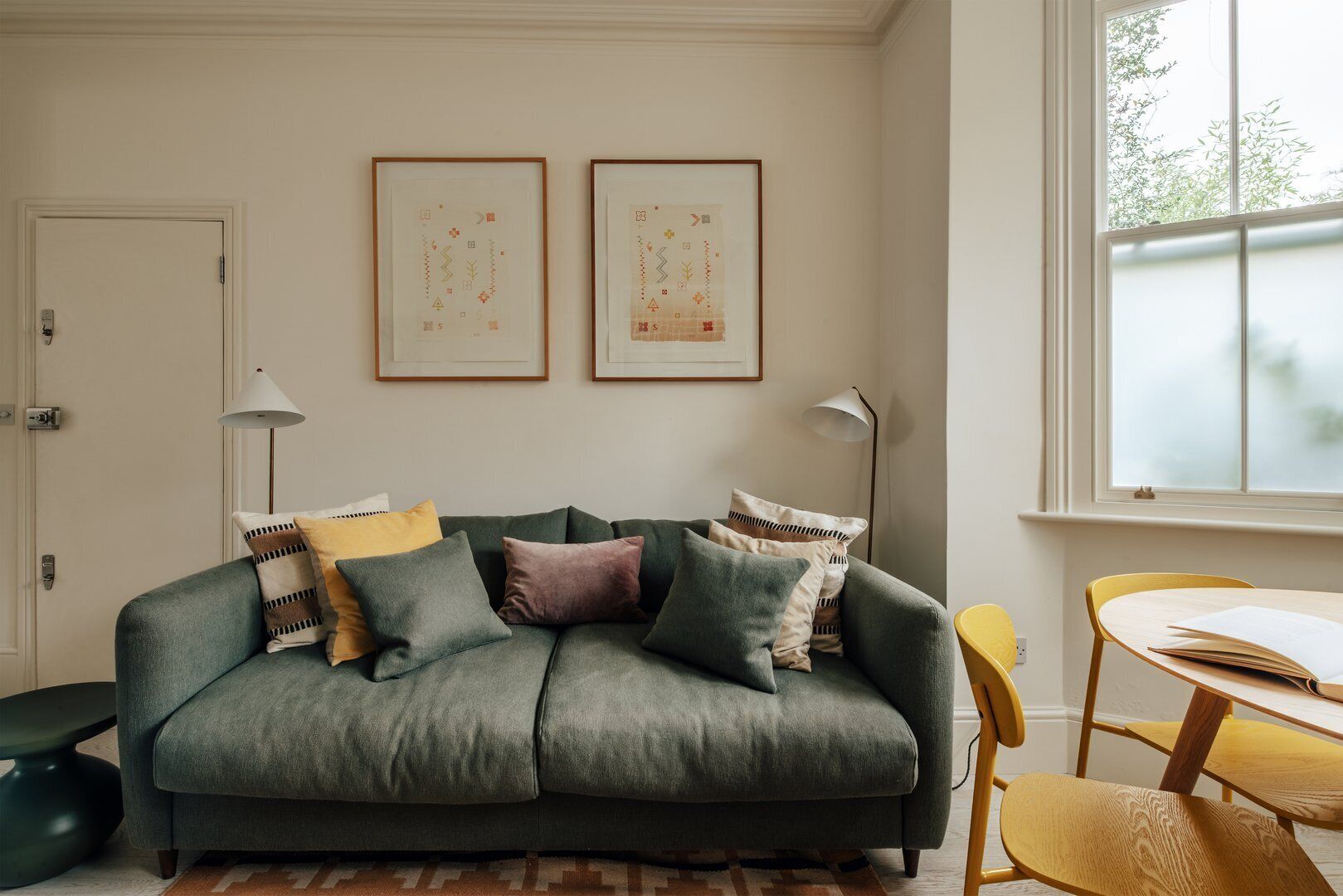 Ein Wohnzimmer mit einem grünen Sofa, einem kleinen runden Tisch und zwei gerahmten abstrakten Kunstwerken an der Wand.