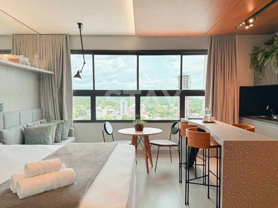 Habitación de hotel moderna con cama, zona de comedor, cocina y ventana grande con vista a la ciudad.