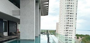 A modern hotel with a rooftop infinity pool overlooking a cityscape and body of water.