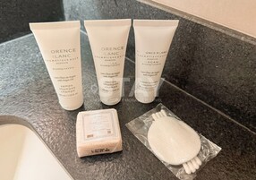Tres tubos de champú Florence Blanc, una pastilla de jabón y un cepillo para el cabello sobre una encimera de baño.