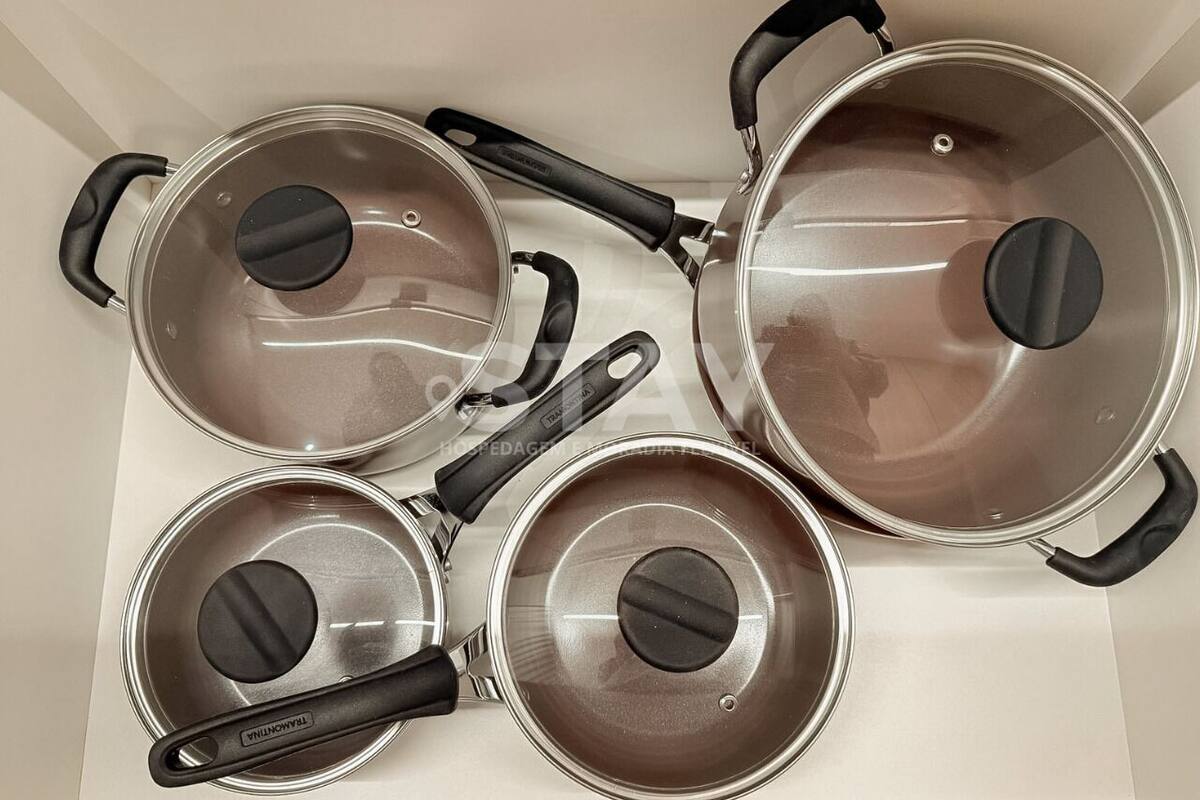 Four stainless steel pots with lids and black handles on a white countertop.