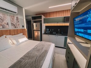 A modern hotel room with a bed, a TV, a kitchenette, and a built-in air conditioning unit.