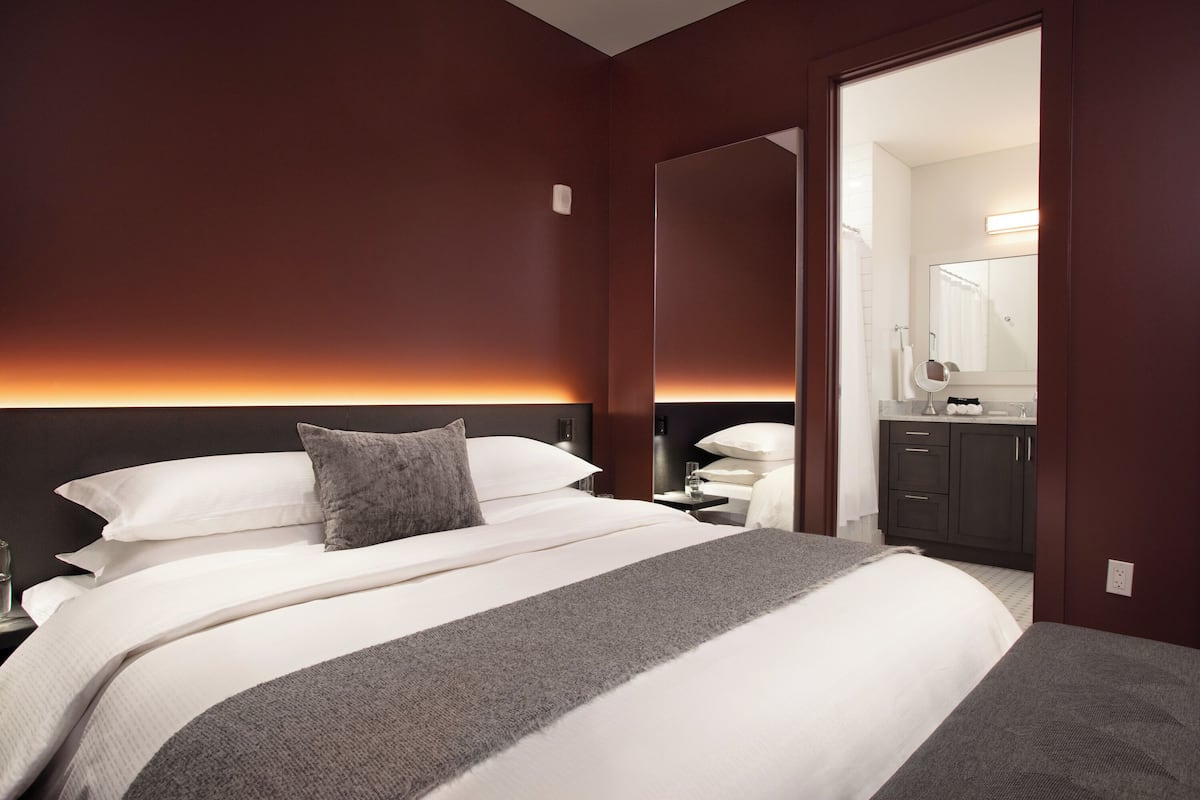 A hotel room with a large bed, a nightstand, a mirror, and a bathroom visible through an open door.