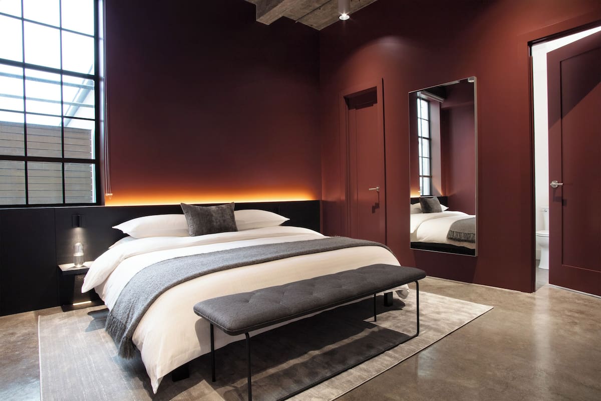 A modern bedroom with a large bed, bedside tables, a bench, and a mirror.